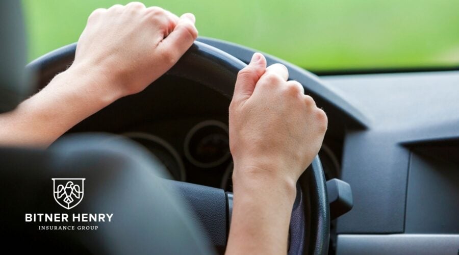 Someone holds onto a steering wheel, the bitner henry logo in the bottom left.