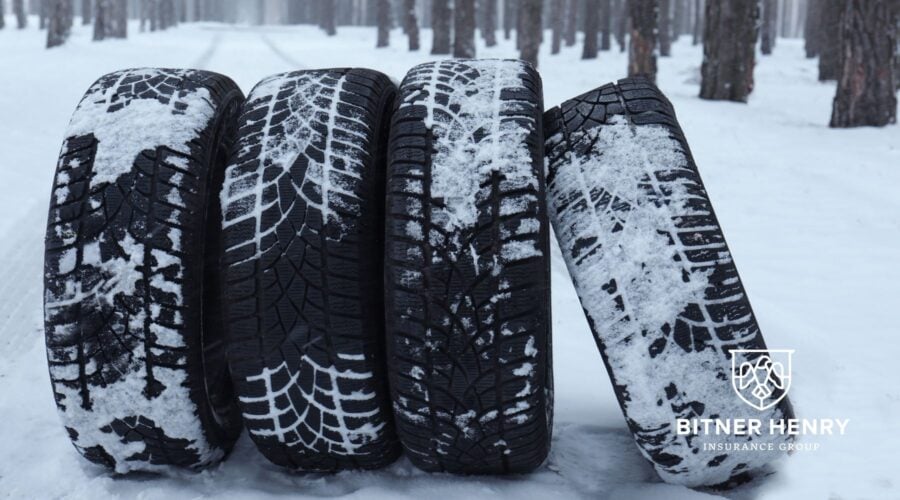 Tires covered in snow lean against each other. The Bitner Henry logo is in the bottom right.