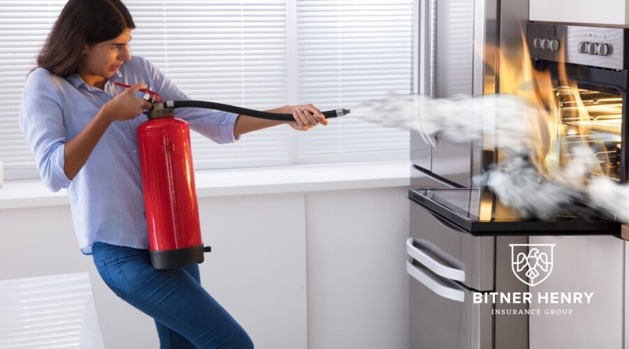 a woman uses a fire extinguisher to put out a fire in an oven. The Bitner Henry logo is there.