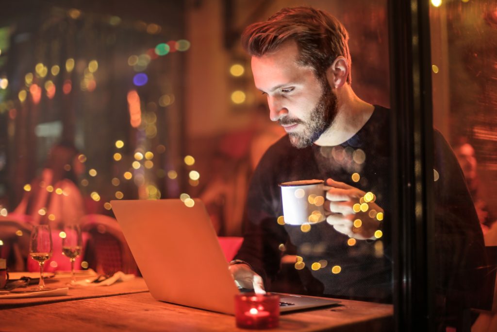 Man sitting in a restaurant drinking coffee and using a laptop 