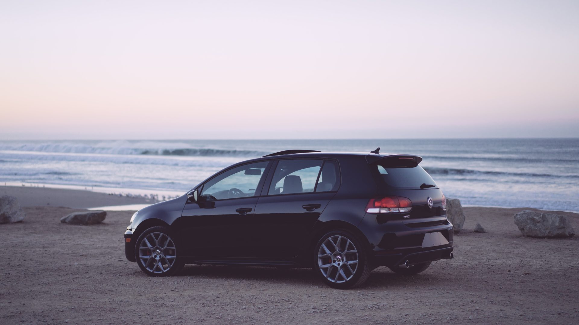 Black Volkeswagen hatchback parked on a beach 