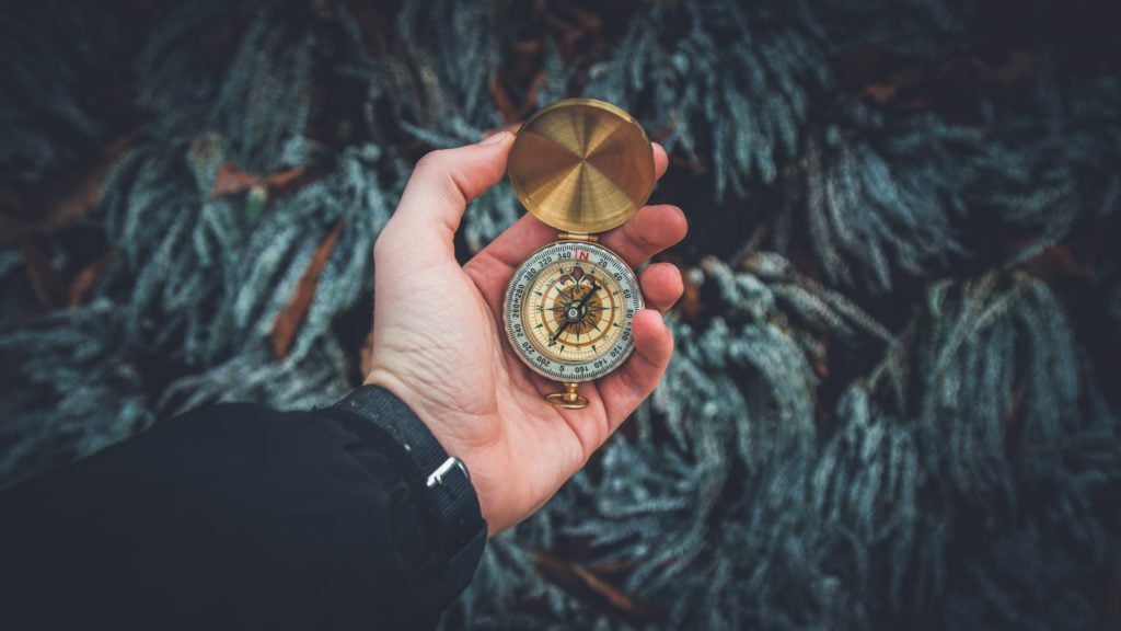 Man holding a gold compass in front of greenery