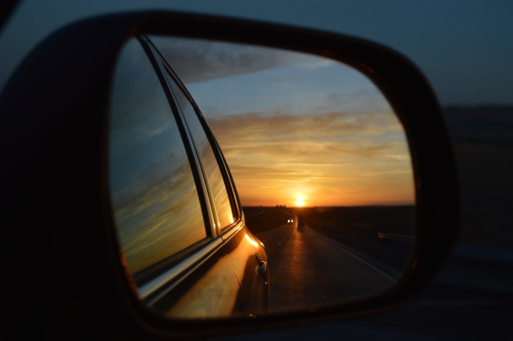 reflection of a sunset in a rear view car mirror