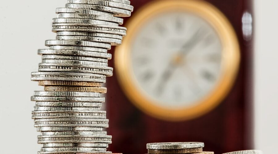 Stacked up coins in front of a clock