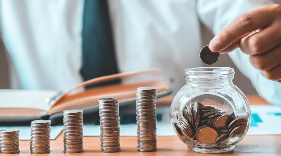 Coins stacking up in a row with a hand placing a coin in a jar.