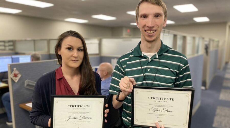 Two young insurance professionals hold certificates of new licenses in office