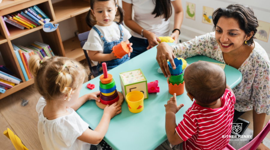 Two childcare employees play with 3 children. The Bitner Henry logo is in the bottom right.
