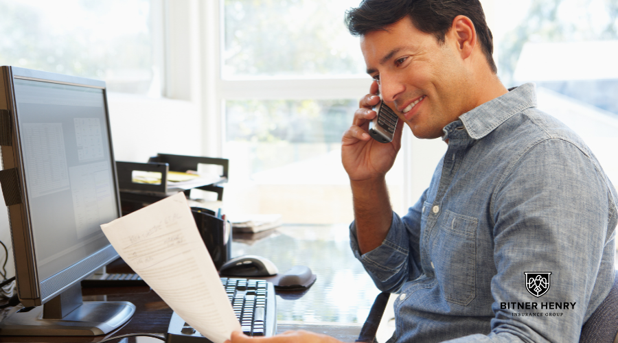 A man studies his insurance policy while on the phone with his agent. The Bitner Henry logo is on the bottom right.