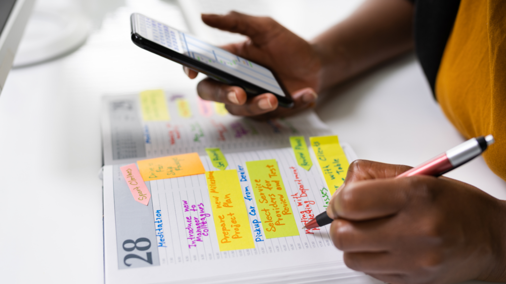 someone holding a pen and phone while writing in a planner