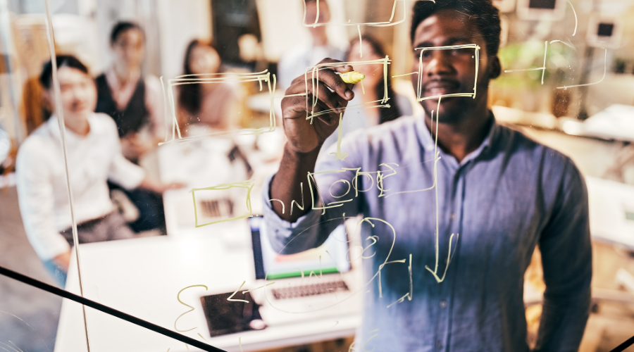 man drawing on glass board with people behind him