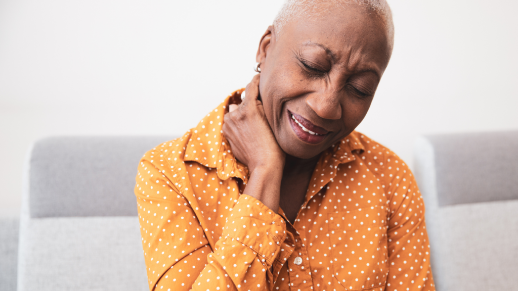 woman in orange shirt holding neck in pain