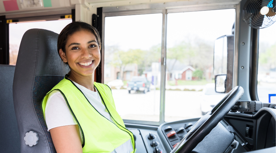 Woman in safety vest behind steering wheel smiling at camera