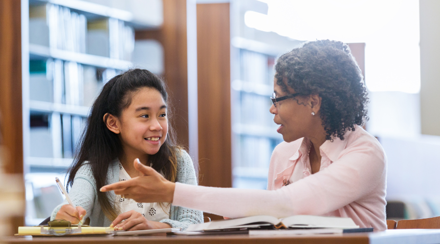 older woman with glasses talking with young girl in a library setting