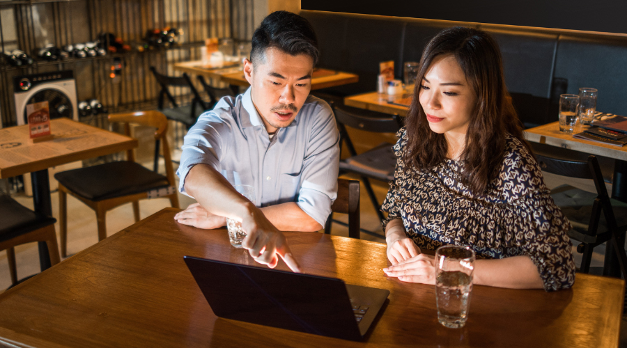 Insurance broker and customer sitting in coffee shop looking at a laptop