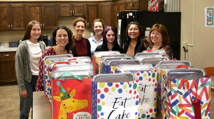 Group of employees standing behind a table filled with birthday bags