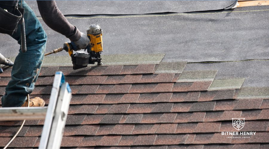 A man installs a roof with a drill. The Bitner Henry logo is on the bottom right.