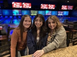 Alexis, Sam,, and Lexi smile at the camera at the bowling alley
