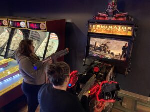 Friends play an arcade game at the bowling alley, smiling brightly