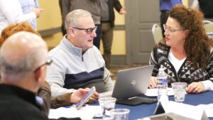 Bruce, Christine, and Darren converse at a table, surrounded by papers