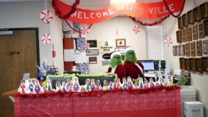The front desk, decked out with Whoville decorations and dressed as two Grinches, smile at the camera.