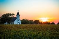 A church stands in a field at sunset.