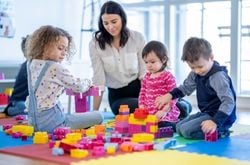 children and a caregiver play blocks A woman plays with colorful blocks with three children