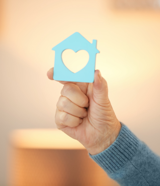 Caring A hand holds up a house with a heart in it