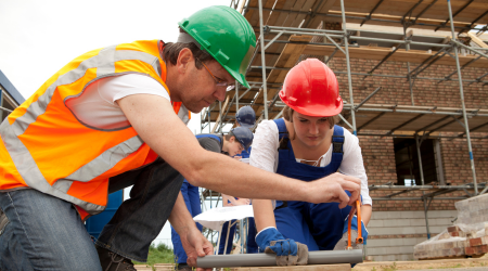 Teacher with Student (1) Two plumbers measure and cut a pipe