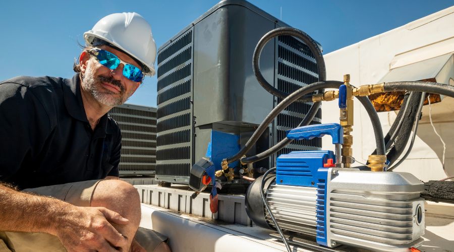 A smiling HVAC employee on a roof with HVAC equipment behind him
