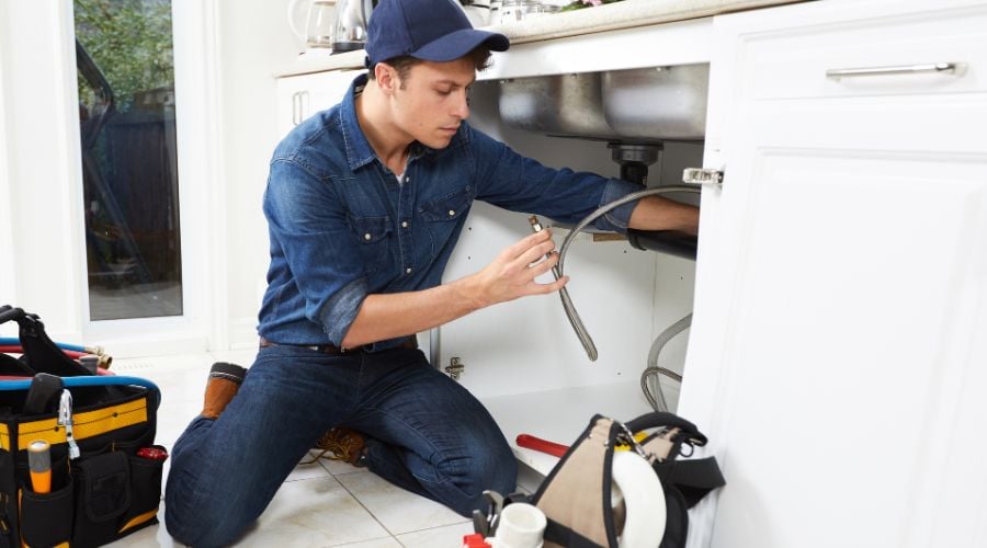 A plumber works under a sink with the pipes.