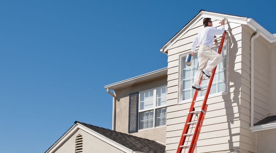 A man paints a house with a stepladder
