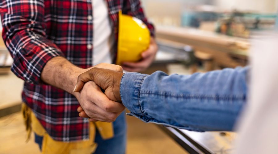 two contractors shake hands. One holds a hard hat