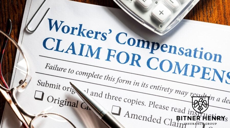 workers' comp claim paper with a pen, calculator, and glasses. the bitner henry logo is in the bottom left