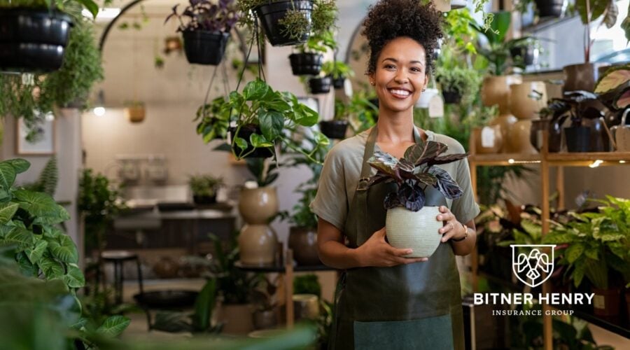 A business owner stands with her plant wares. The Bitner Henry logo is in the bottom right.