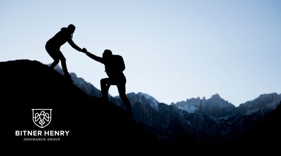 a woman helps a man up a mountain, serving him and helping him. The Bitner Henry logo is in the bottom left.