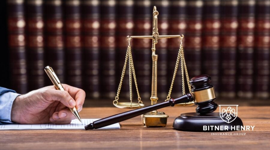 A lawyer writes on a paper. A set of scales and a gavel rest on the table. The Bitner Henry logo was in the bottom right.