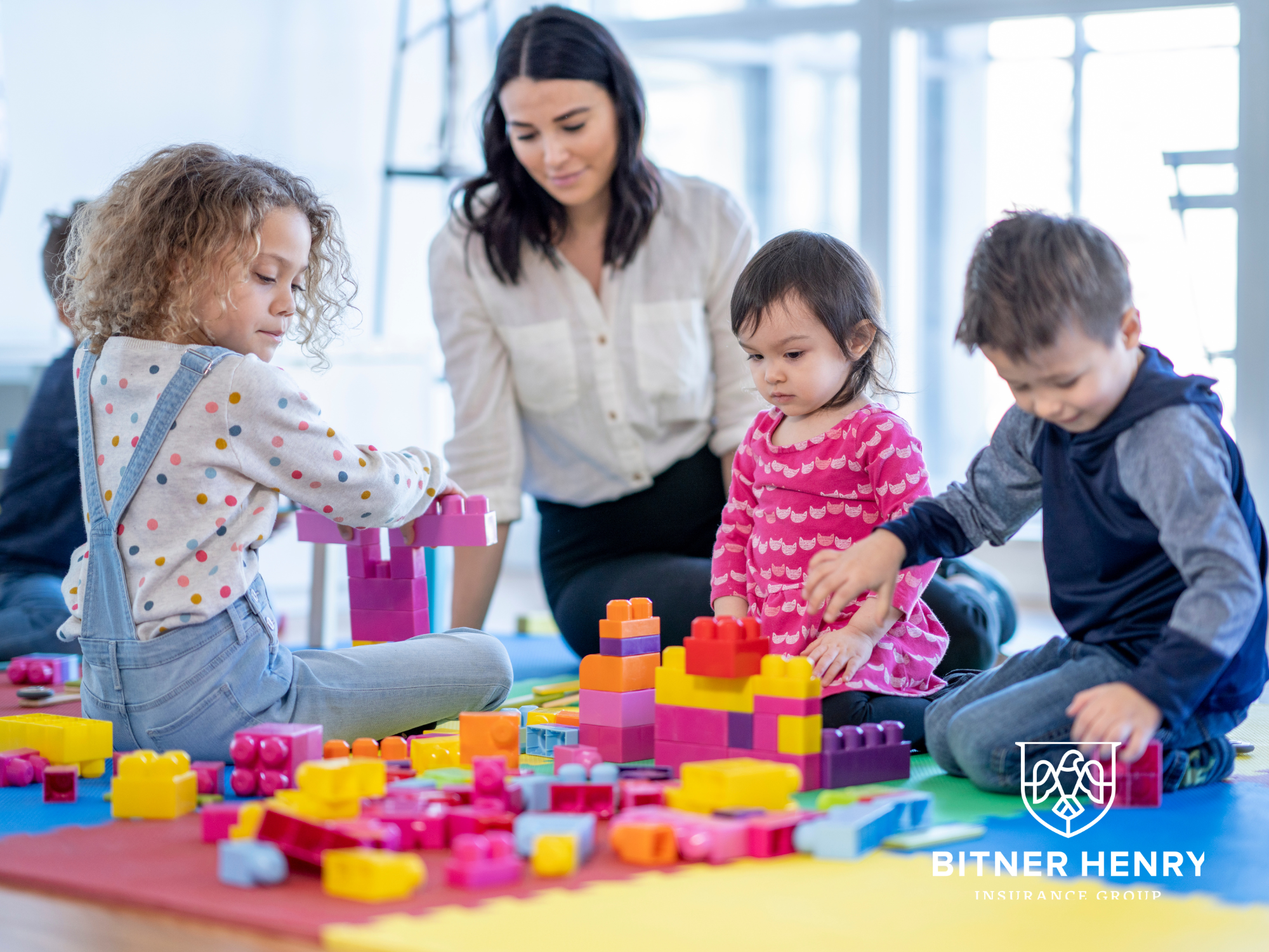 A teacher plays with some children with building blocks in a childcare environment.