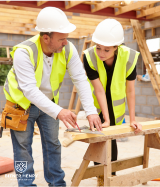Two carpenters in safety vests discuss a piece of wood