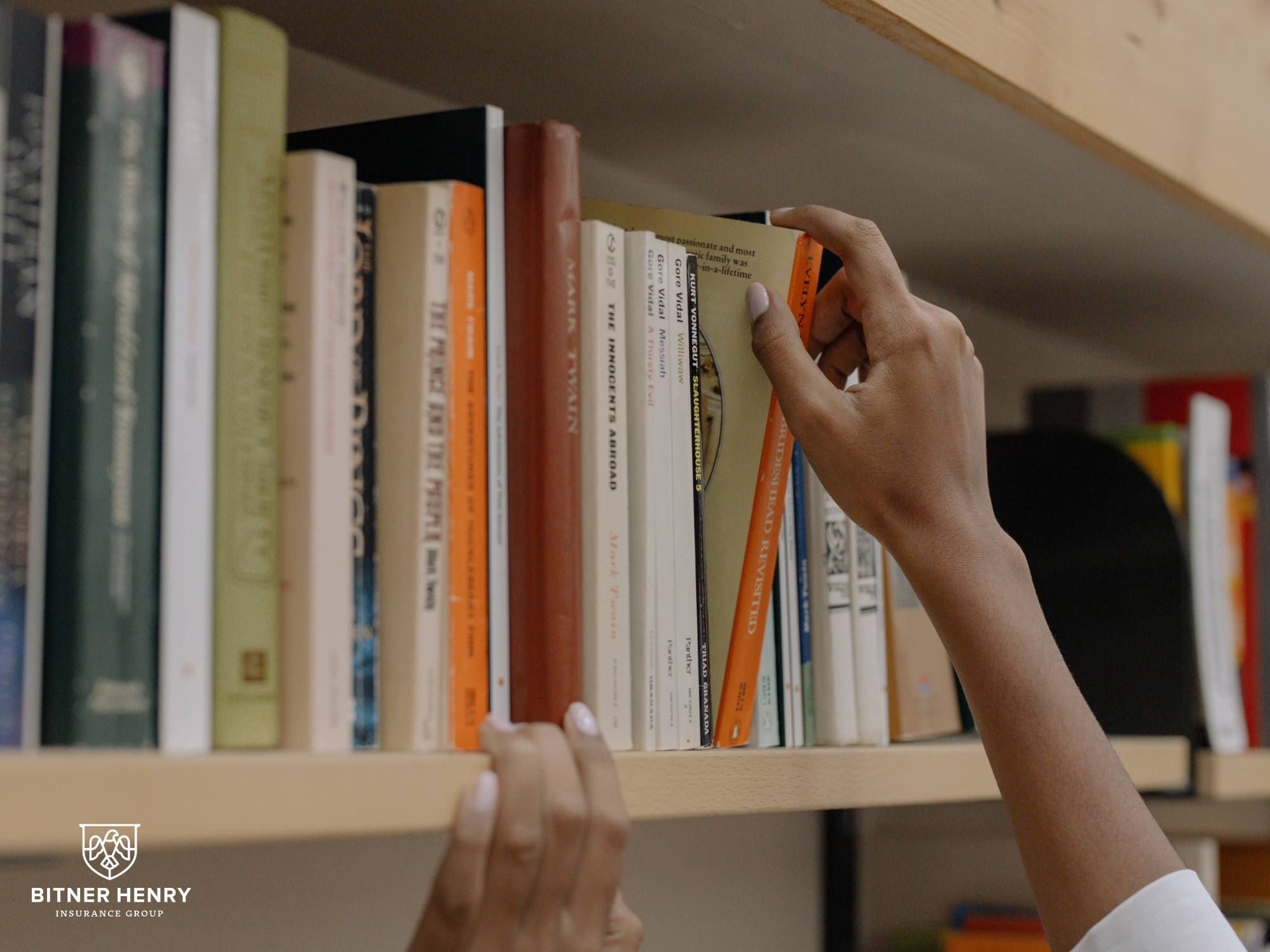 Reaching to a bookshelf to get resources, with the bitner henry logo in the bottom right.