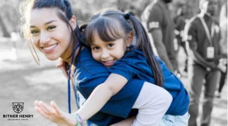 A volunteer for a nonprofit gives a child a piggyback ride. The Bitner Henry logo is in the bottom left.