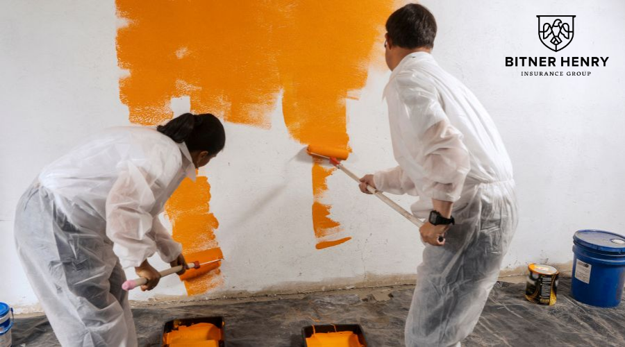 Two painters use paint rollers to paint a wall orange